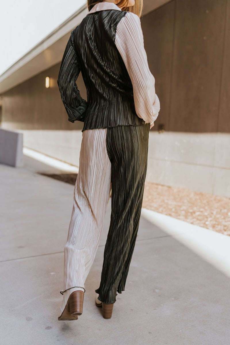Back view of model wearing the Block It Out Pants that have olive and cream color block coloring, plisse fabric, two front pockets, and elastic waistband, and flare wide legs with lettuce hems.