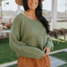 Close up view of model wearing the Chasing The Spotlight Sweater which features dark sage cable knit fabric, v neckline, and long sleeves with cable knit wrists.