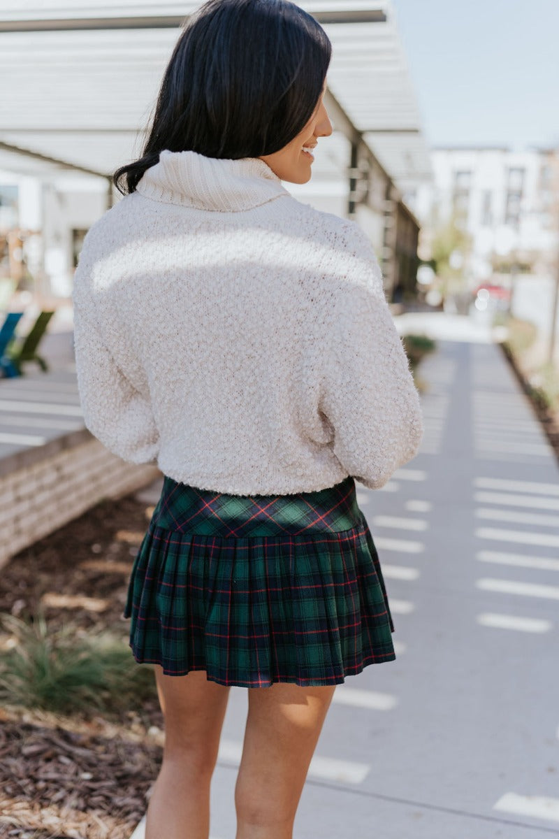 Back view of model wearing the Days Go By Sweater In Cream that has cream ribbed knit fabric on the front, a loose turtleneck, popcorn detailing on the back and sleeves, and long sleeves.