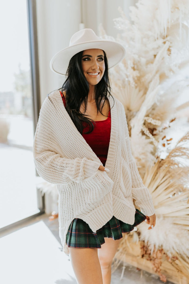 Front view of the Snow Cozy Cardigan featuring cream chenille fabric, cable knit pattern, two front pockets, side slits on the hem, and long sleeves with cuffs.