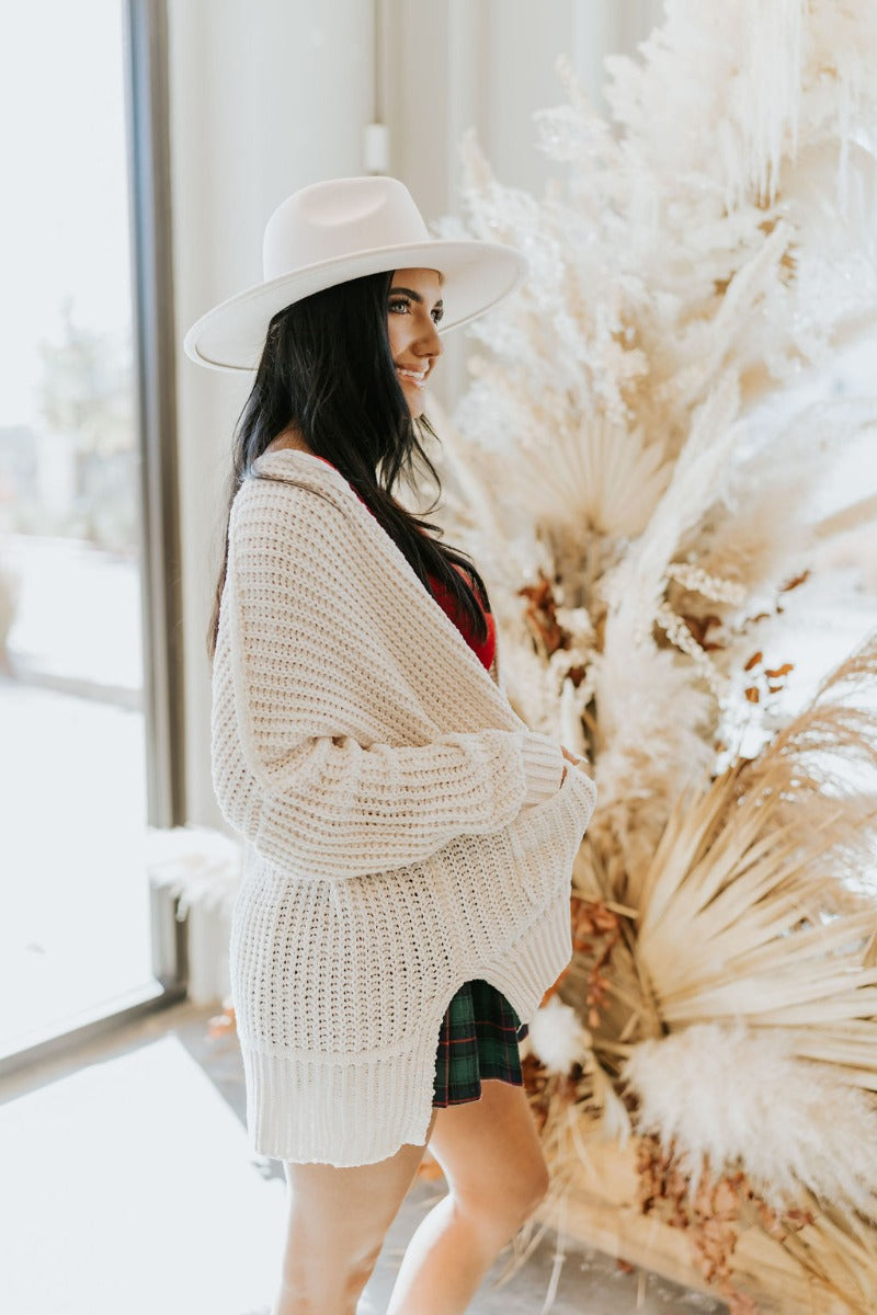 Side view of the Snow Cozy Cardigan featuring cream chenille fabric, cable knit pattern, two front pockets, side slits on the hem, and long sleeves with cuffs.