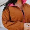 Close up view of model wearing the Floral Daze Quilted Jacket that features camel colored fabric with a stitched flower pattern, a gold zip up, a pink lining, a high collar neckline, and long balloon sleeves with cuffs