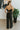 Back view of The Fresh Eyes Jumpsuit features black fabric, sweetheart neckline with a v wire, feather details, adjustable spaghetti straps, tie around the waist, two front pockets, back zipper, open back and flare pant leg.