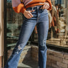 Front view of model wearing the Vervet: Let's Go Cropped Flares that have dark blue denim fabric, distressing, a frayed hem, a high-rise waist, mid flares, two front pockets, two back pockets, and a button and zipper closure