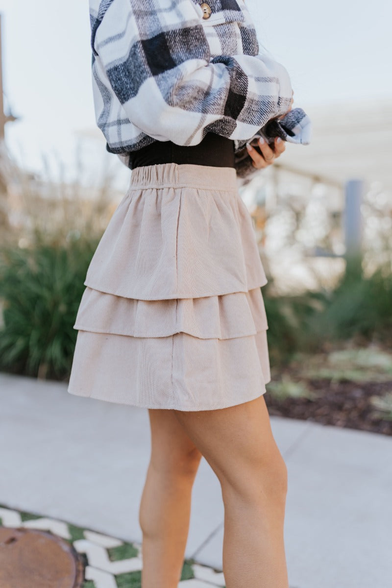 Side view of model wearing the Lexington Corduroy Skirt in Cream that has cream corduroy fabric, ruffle tiered details, a mini length hem, and an elastic waist band