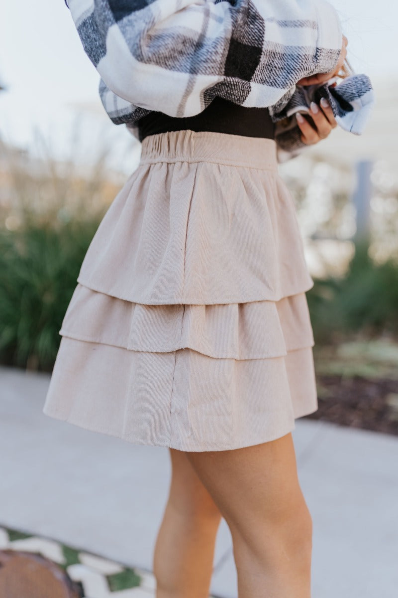 Side view of model wearing the Lexington Corduroy Skirt in Cream that has cream corduroy fabric, ruffle tiered details, a mini length hem, and an elastic waist band