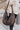 Close view of model holding the Checked Out Bag In Black that has black plush fabric with stitched squares, a black zipper closure, an inner zippered pockets, and two inner open pockets.