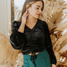 Front view of model wearing the The Late Nights Velvet Top that has  black velvet fabric, a cropped waist, ruched front detailing, a  v neckline, and long sleeves with elastic wrists.
