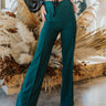 Front view of model wearing the Let's Chat Pants in Emerald that have emerald green fabric, a seam down each front leg, a slight v waistline, a back zipper closure, and wide legs