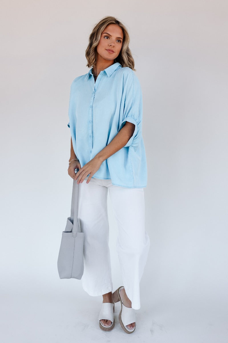 Full body view of model wearing the Grace Washed Light Blue Short Sleeve Top which features light washed blue tencel fabric, monochrome front button up closure, collared neckline and short sleeves.