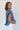 Side view of model wearing the Allison Washed Denim Ruffle Short Sleeve Top which features washed denim fabric, slight slits on each side, round collar with v-neckline and short sleeves with ruffle hem.