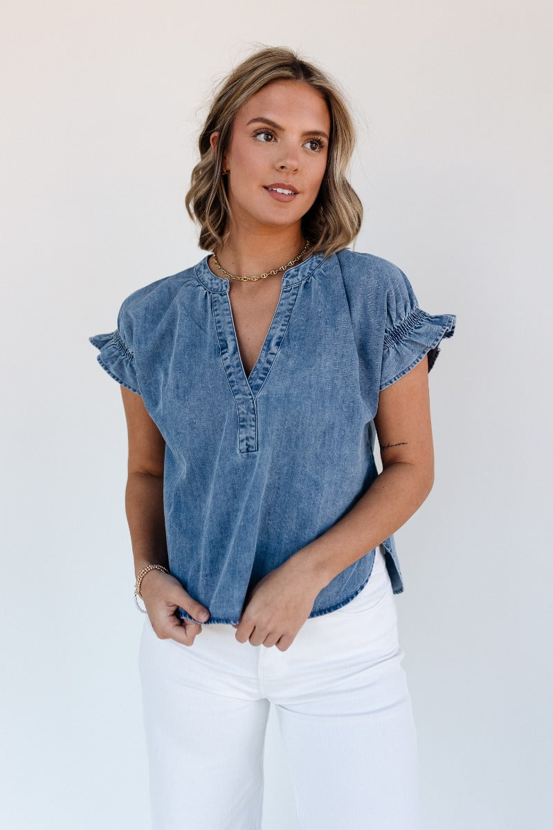 Close up view of model wearing the Allison Washed Denim Ruffle Short Sleeve Top which features washed denim fabric, slight slits on each side, round collar with v-neckline and short sleeves with ruffle hem.