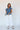Full body view of model wearing the Allison Washed Denim Ruffle Short Sleeve Top which features washed denim fabric, slight slits on each side, round collar with v-neckline and short sleeves with ruffle hem.