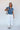 Full body view of model wearing the Allison Washed Denim Ruffle Short Sleeve Top which features washed denim fabric, slight slits on each side, round collar with v-neckline and short sleeves with ruffle hem.