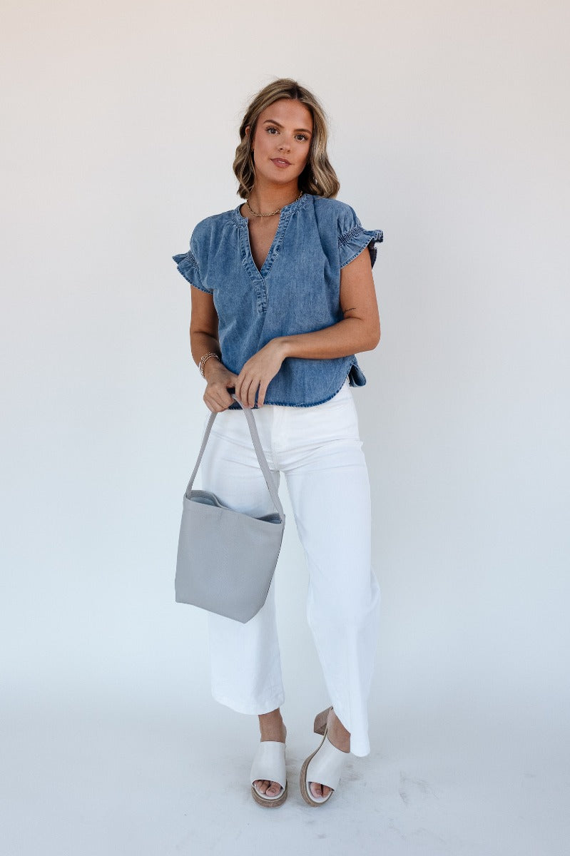 Full body view of model wearing the Allison Washed Denim Ruffle Short Sleeve Top which features washed denim fabric, slight slits on each side, round collar with v-neckline and short sleeves with ruffle hem.