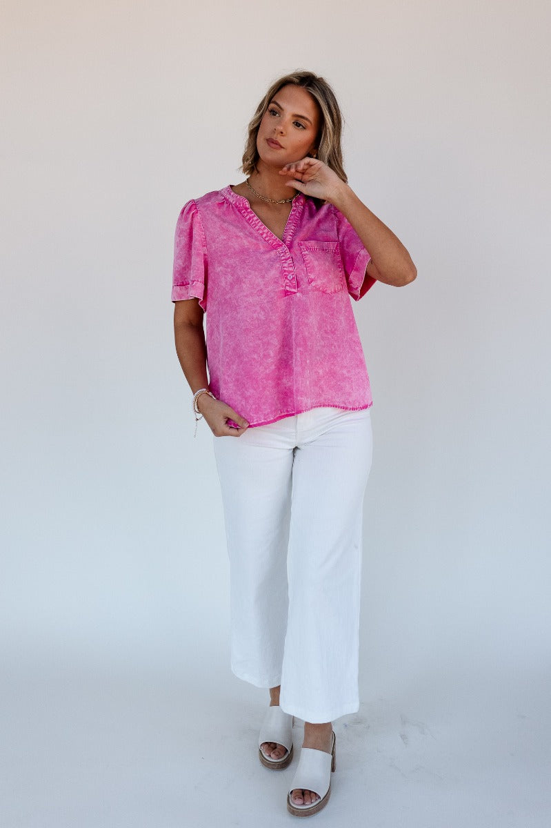Full body view of model wearing the Ashlyn Washed Pink Short Sleeve Top which features washed pink tencel fabric, a scooped hem, a front left chest pocket, a monochrome quarter button-up v-neckline, and short sleeves.