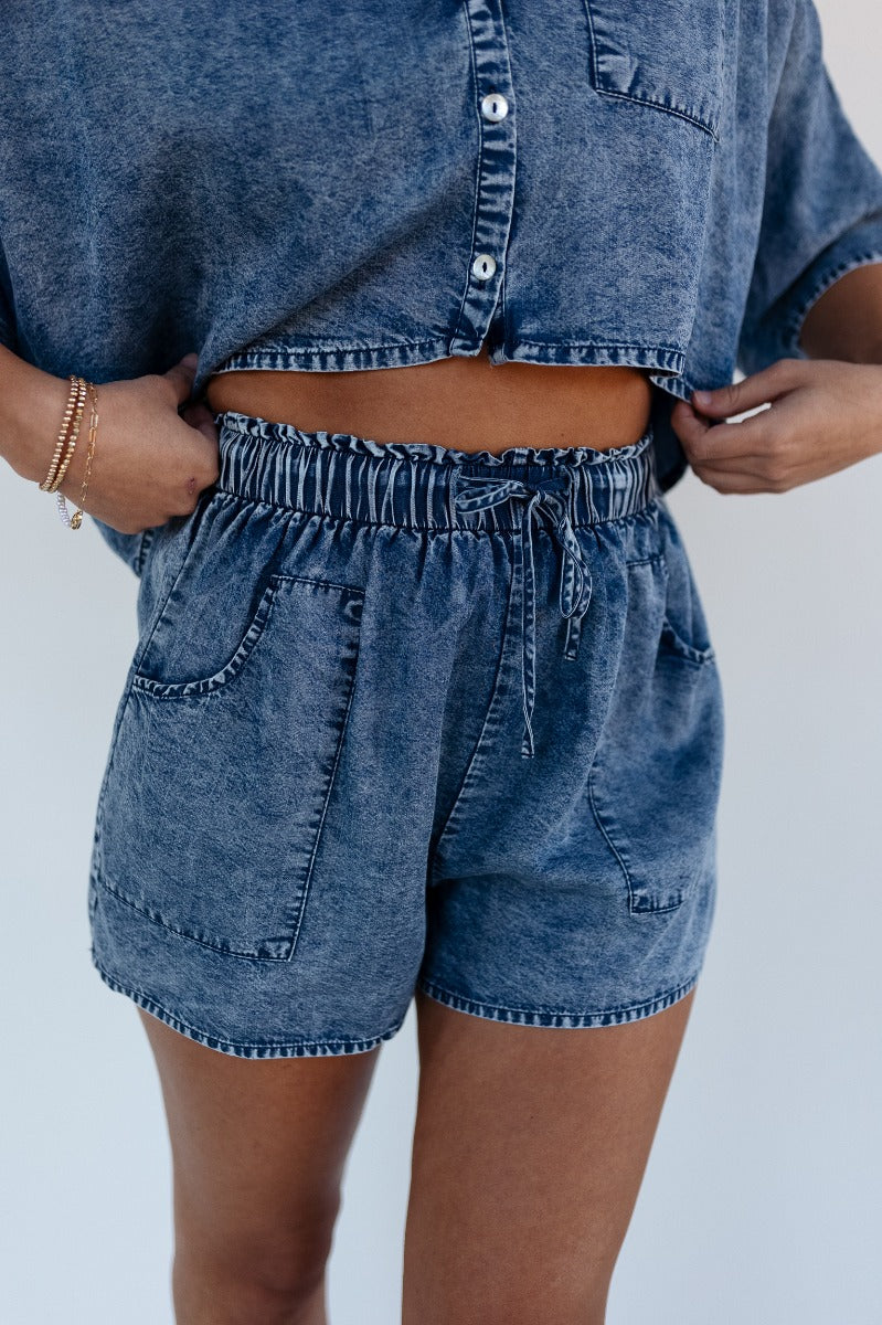 Front view of model wearing the Jade Washed Denim Elastic Shorts which features washed denim tencel fabric, two front pockets and elastic waistband wih drawstring ties.