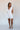 Full body front view of model wearing the Peyton Off White Denim Sleeveless Romper that has off white cotton fabric, two front pockets, a plunge neck, ruffle straps, and a back zipper with a hook closure.