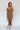 Full body front view of model wearing the Liliana Brown Asymmetrical Sleeveless Midi Dress that has light brown knit fabric, an asymetrical ruffle hem, midi length, square neckline, adjustable straps and sleeveless.