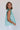 Side view of model wearing the Emory Aqua Sleeveless Ruffle Top that has aqua blue cotton fabric, a ruffled notched neckline with ties, and a sleeveless body with ruffle details.