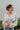 Frontal view of the Auburn Avenue Top that features an ivory colored material, a V neckline with a button closure, a long pleated sleeve, a smocked bottom with a ruffle hem, and a back tie closure.