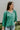 Frontal view of the In Charge Top that features a green colored material, a round neck with an adjustable tie closure, a notched neckline, a long sleeve, and a flowy fit.