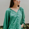 Frontal view of the In Charge Top that features a green colored material, a round neck with an adjustable tie closure, a notched neckline, a long sleeve, and a flowy fit.