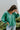 Frontal view of the In Charge Top that features a green colored material, a round neck with an adjustable tie closure, a notched neckline, a long sleeve, and a flowy fit.