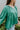 Frontal view of the In Charge Top that features a green colored material, a round neck with an adjustable tie closure, a notched neckline, a long sleeve, and a flowy fit.