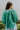 Back view of the In Charge Top that features a green colored material, a round neck with an adjustable tie closure, a notched neckline, a long sleeve, and a flowy fit.
