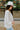 Side view of the In Charge Top In Ivory that features an ivory colored material, a round neck with an adjustable tie closure, a notched neckline, a long sleeve, and a flowy fit.