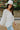 Side view of the In Charge Top In Ivory that features an ivory colored material, a round neck with an adjustable tie closure, a notched neckline, a long sleeve, and a flowy fit.