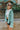 Frontal/ Side view of the Sloane Corduroy Shacket that features a jade green corduroy material, a collar neckline, a button-up front, a front pocket, and long cuffed sleeves.