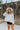 Front view of model wearing the Love Always Top, which has an ivory colored material, a round neck, a 3/4 button-up front, a long sleeve, front lace detail, a babydoll design, and a flowy fit