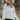Front view of model wearing the Love Always Top, which has an ivory colored material, a round neck, a 3/4 button-up front, a long sleeve, front lace detail, a babydoll design, and a flowy fit