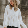 Front view of model wearing the Love Always Top, which has an ivory colored material, a round neck, a 3/4 button-up front, a long sleeve, front lace detail, a babydoll design, and a flowy fit