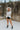 Full body front view of model wearing the Love Always Top, which has an ivory colored material, a round neck, a 3/4 button-up front, a long sleeve, front lace detail, a babydoll design, and a flowy fit