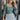 Frontal view of the Wait A Minute Top that features a green colored material, a straight neckline, a long sleeve with a ruffle trim at the wrist, a pleated front, and a smocked back.