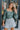 Frontal view of the Wait A Minute Top that features a green colored material, a straight neckline, a long sleeve with a ruffle trim at the wrist, a pleated front, and a smocked back.