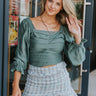 Frontal view of the Wait A Minute Top that features a green colored material, a straight neckline, a long sleeve with a ruffle trim at the wrist, a pleated front, and a smocked back.