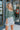 Frontal view of the Wait A Minute Top that features a green colored material, a straight neckline, a long sleeve with a ruffle trim at the wrist, a pleated front, and a smocked back.