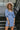 Frontal view of the Washed Away Mini Dress that features a washed blue material, a straight neckline with a ruffle trim, a 3/4 sleeve, a smocked top and back, and a mini length.