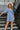 Frontal view of the Washed Away Mini Dress that features a washed blue material, a straight neckline with a ruffle trim, a 3/4 sleeve, a smocked top and back, and a mini length.