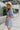 Side view of the Washed Away Mini Dress that features a washed blue material, a straight neckline with a ruffle trim, a 3/4 sleeve, a smocked top and back, and a mini length.