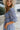 Side view of the Washed Away Mini Dress that features a washed blue material, a straight neckline with a ruffle trim, a 3/4 sleeve, a smocked top and back, and a mini length.