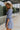 Side view of the Washed Away Mini Dress that features a washed blue material, a straight neckline with a ruffle trim, a 3/4 sleeve, a smocked top and back, and a mini length.