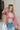 Frontal view of the Say No More Top that features a pink satin material, a monochromatic polka dot print, a collar neckline, a button-up front, a long cuffed sleeve with buttons on the wrists, and a rounded hem with side slits.