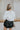 Back view of the Don't Get It Twisted Jacket that features a white faux leather material, a collar neck, a button-up front, a monochromatic white checkered print, front fringe detailing, and a cropped fit.