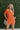 Frontal view of the Spur The Moment Denim Romper that features an orange denim material, a surplice neckline that snaps with a collar, half-length sleeves, a front zipper, pockets, pleating on the legs, and a 3" inseam.
