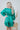 Back view of the A Vision Mini Dress that features a green satin material, a monochromatic floral print, a V neckline, a long puffy sleeve, button detailing at the front, a zipper back closure, and a flowy fit.